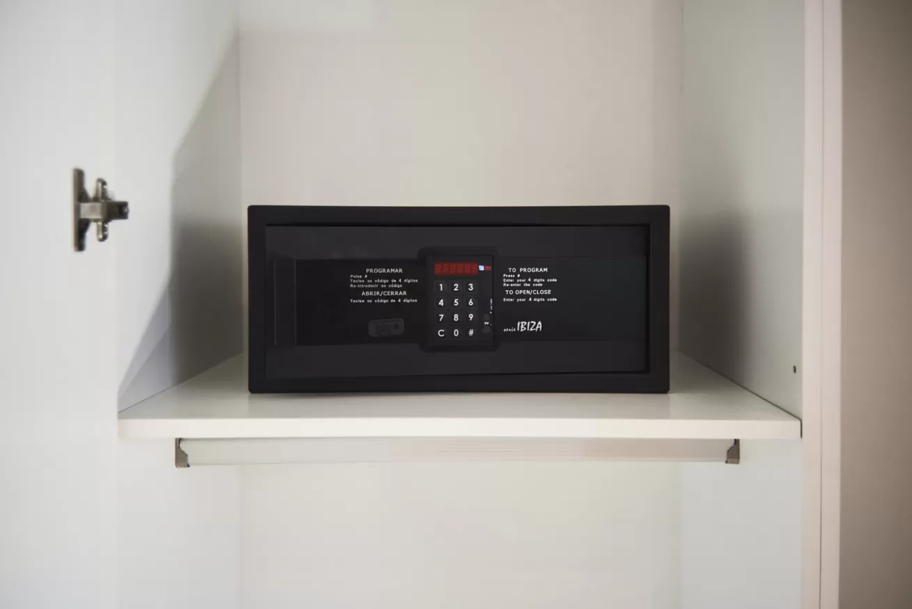 Una caja fuerte negra de pared sobre un estante blanco dentro de un armario o mueble.