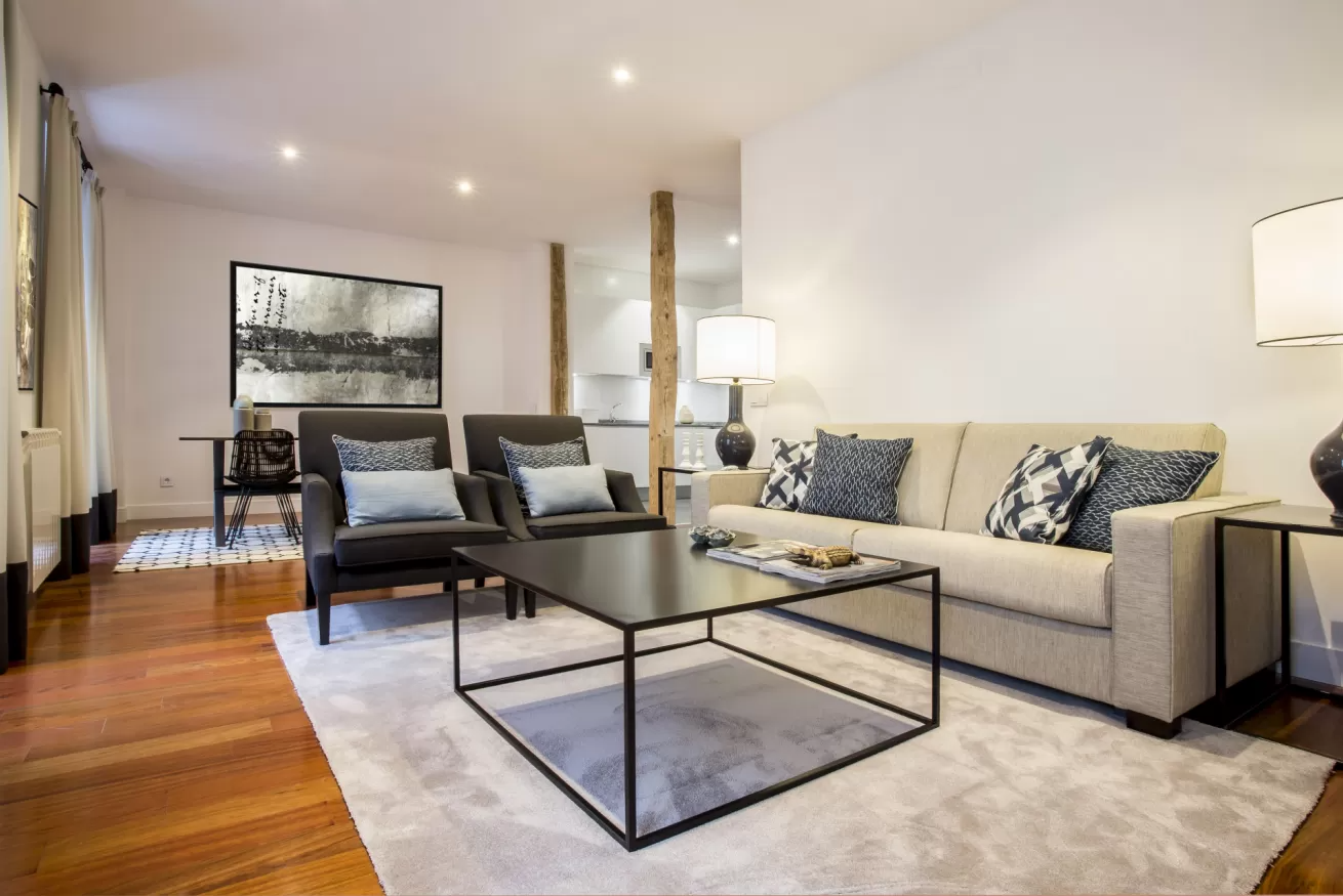 Sala de estar moderna con sofá beige, mesa de centro de cristal, sillas estampadas y suelos de madera noble.