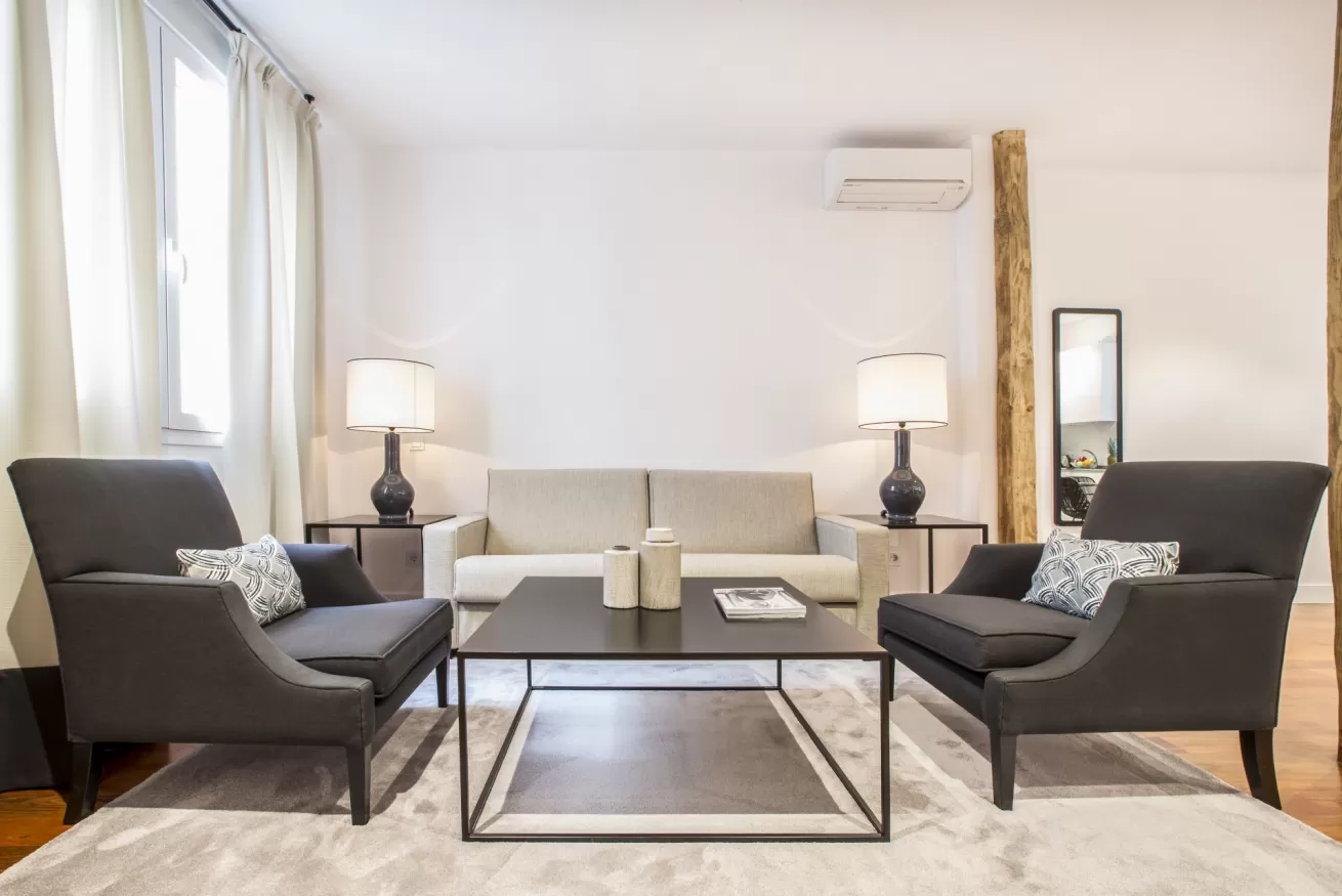 Sala de estar moderna con sillas grises, sofá blanco, lámparas y mesa de centro sobre una alfombra.