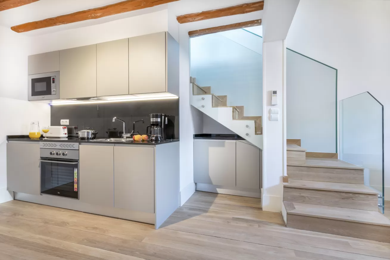 Interior moderno con cocina abierta y escalera, suelos de madera clara y paredes blancas.