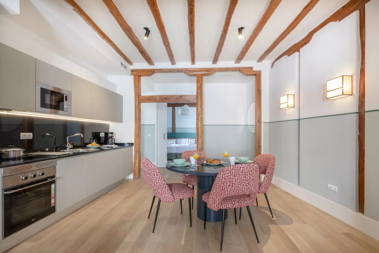 Cocina-comedor moderna con sillas rosas, mesa de cristal y vigas de madera a la vista.