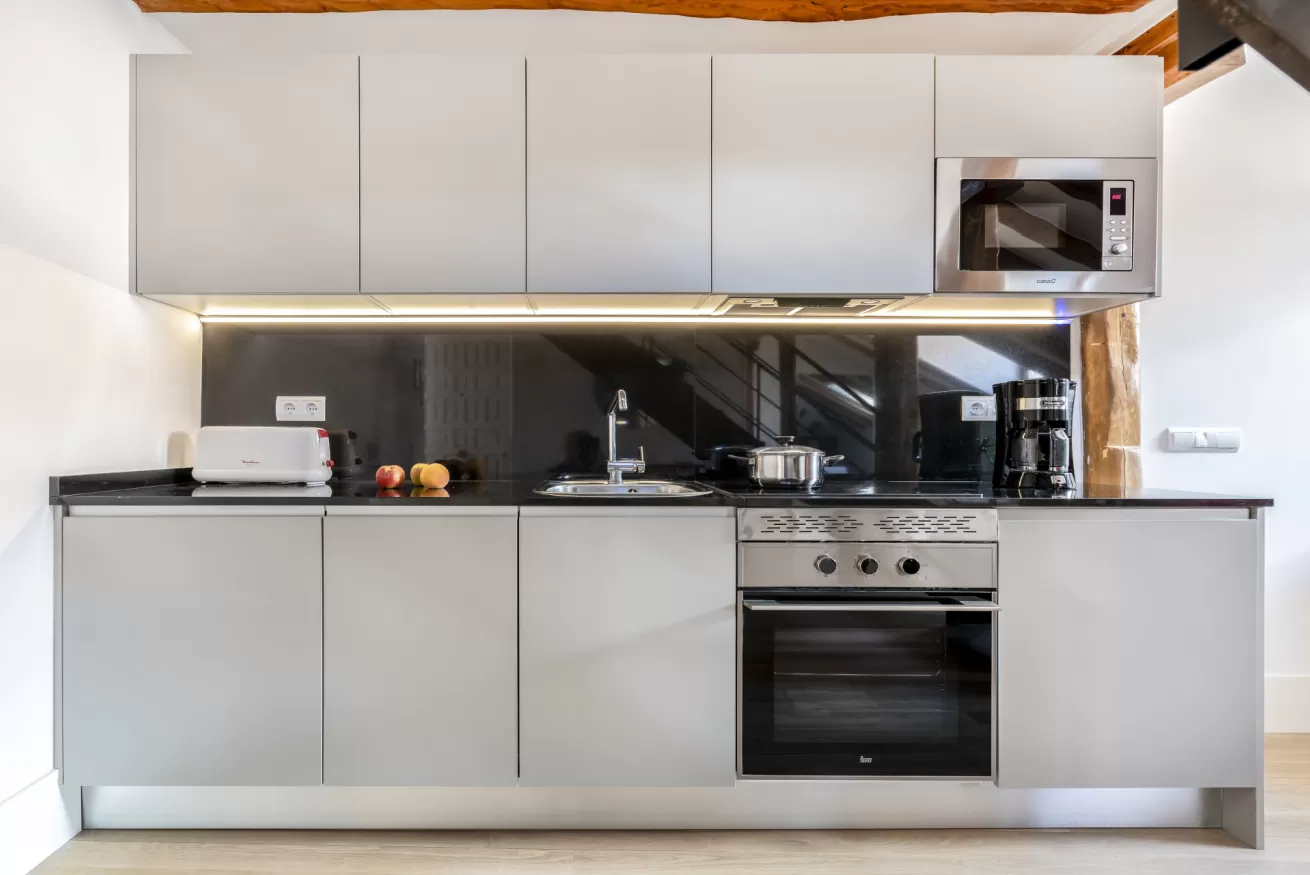 Cocina moderna con gabinetes blancos, protector contra salpicaduras negro, horno de acero inoxidable y microondas.