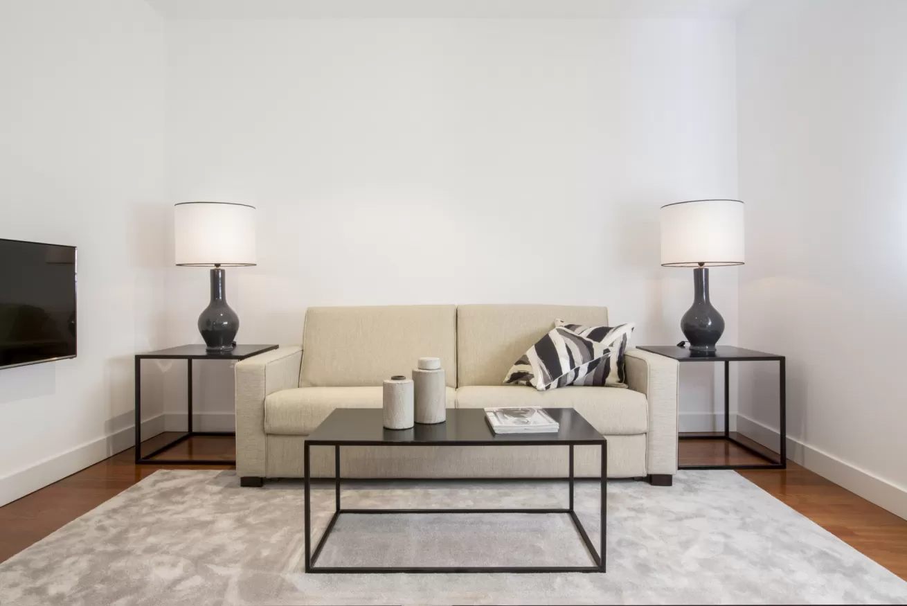 Sala de estar minimalista con sofá beige, mesa de centro negra y mesas auxiliares a juego con lámparas.