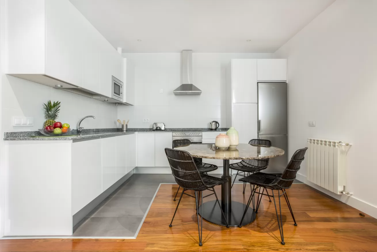 Cocina moderna de color blanco con electrodomésticos de acero inoxidable y una mesa de comedor redonda negra.
