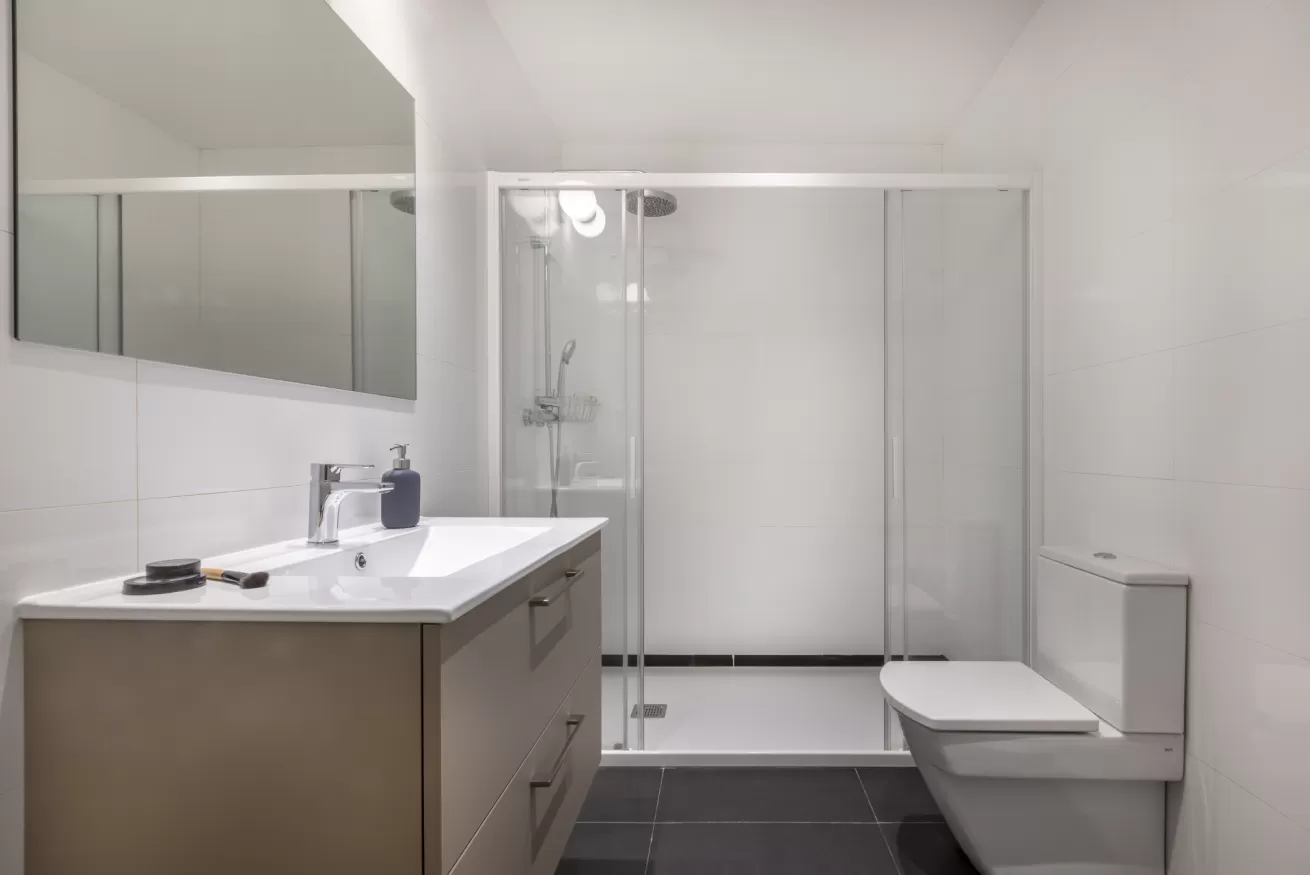 Baño moderno de color blanco con lavabo, espejo, ducha de cristal e inodoro.