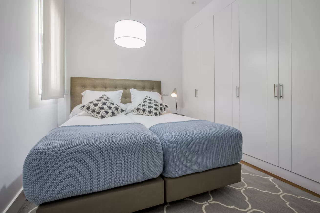 Habitación luminosa con una cama doble bien hecha, armarios blancos y una lámpara de techo colgante.