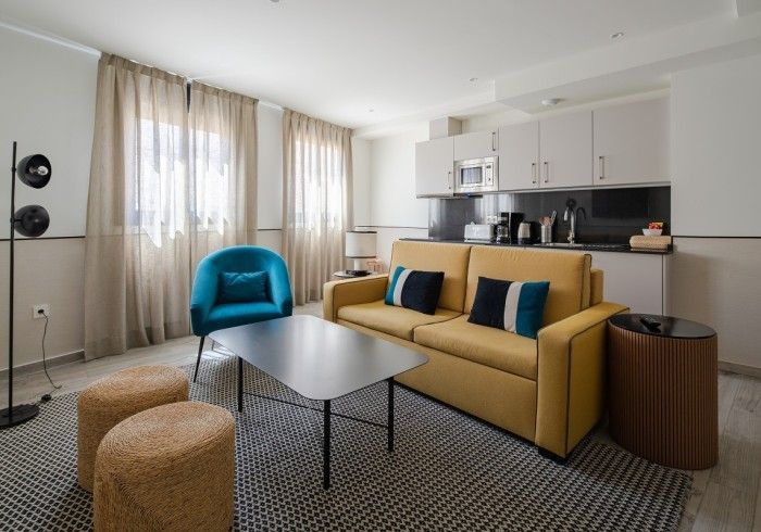 Sala de estar moderna y luminosa con sofá color mostaza, sillón azul, mesa de centro y encimera de cocina.