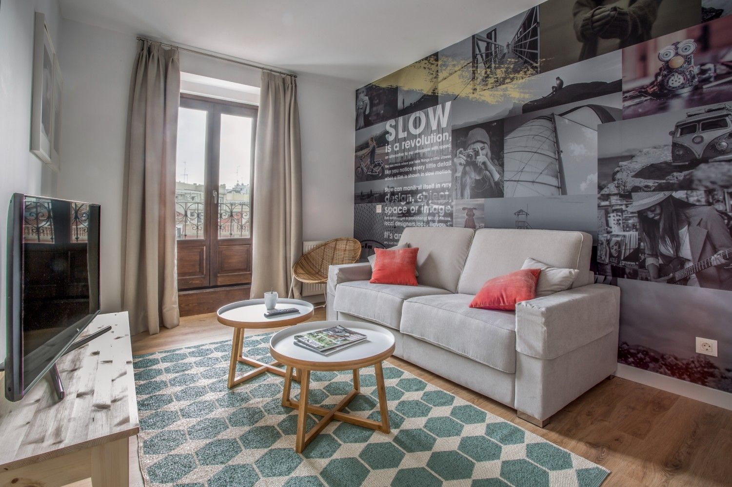 Sala de estar moderna con sofá gris, alfombra estampada, mesas de centro y mural de la ciudad en la pared.