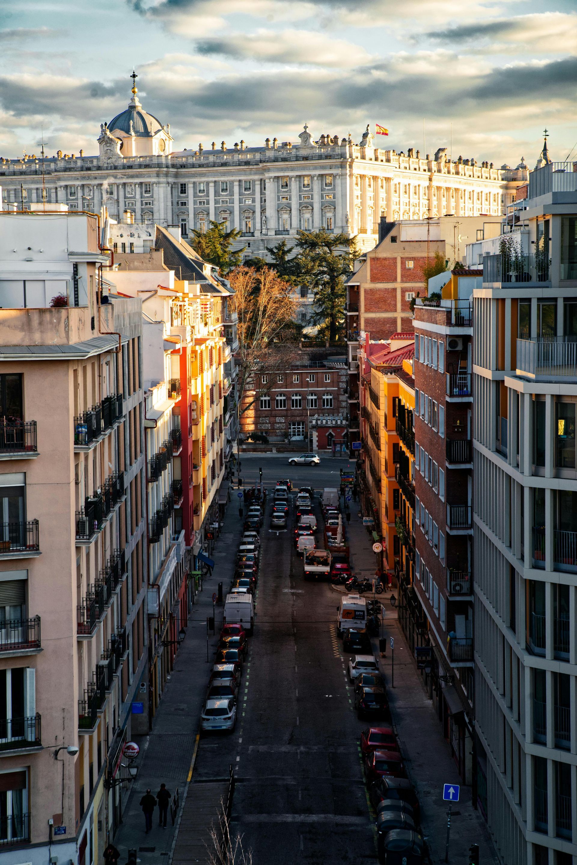 Calle soleada de la ciudad, bordeada de edificios, que conduce hacia un monumento de cúpula blanca en la distancia.