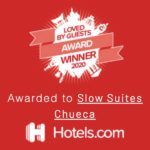Insignia de Hotels.com sobre fondo rojo: “Ganador del premio Loved by Guests 2024” para Slow Suites Chueca.