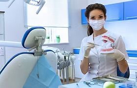 Dentist in a mask and gloves holding a model of teeth in a dental office.