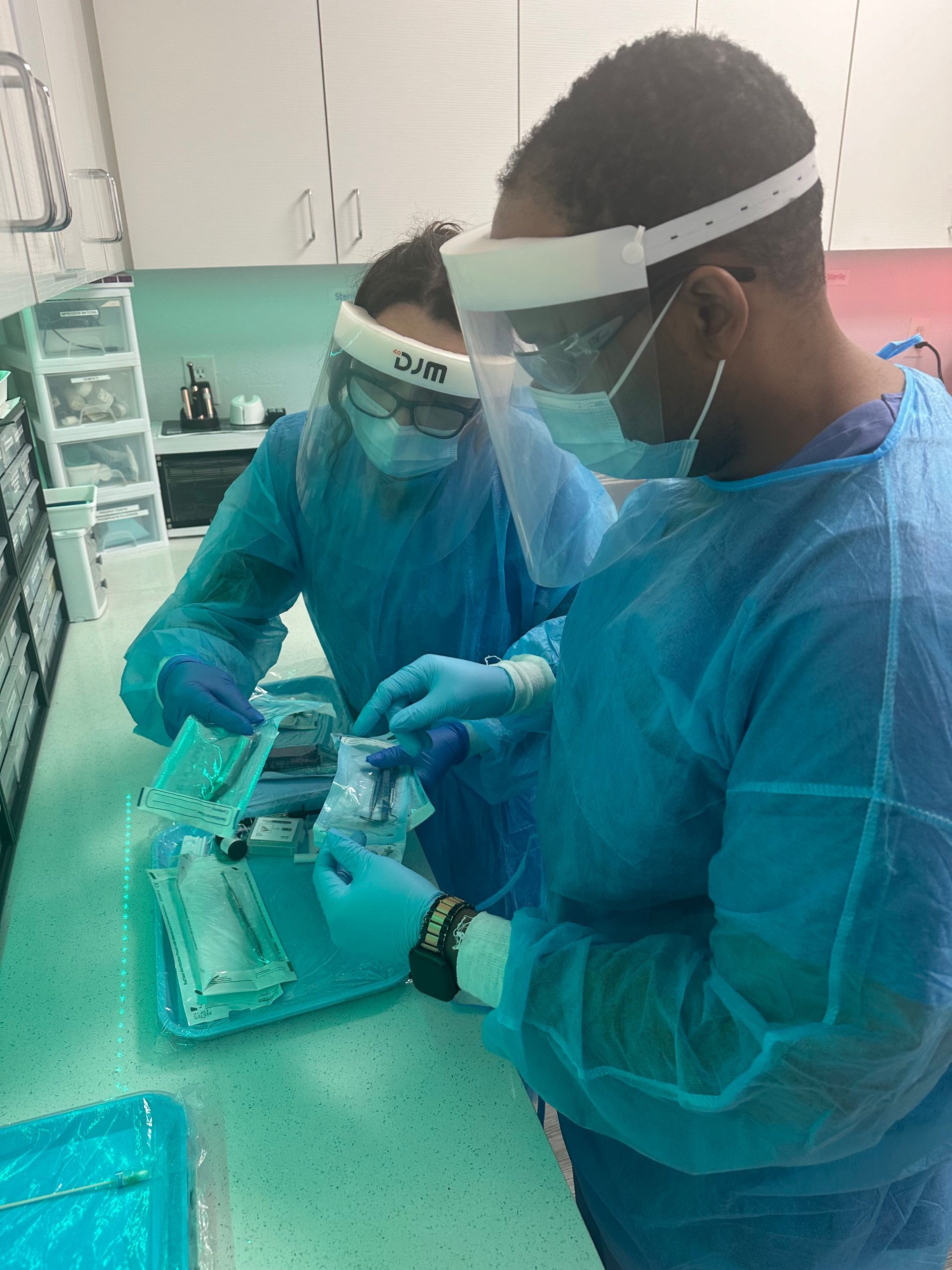 Two people in medical scrubs, masks, and face shields preparing medical tools in a clinic setting.