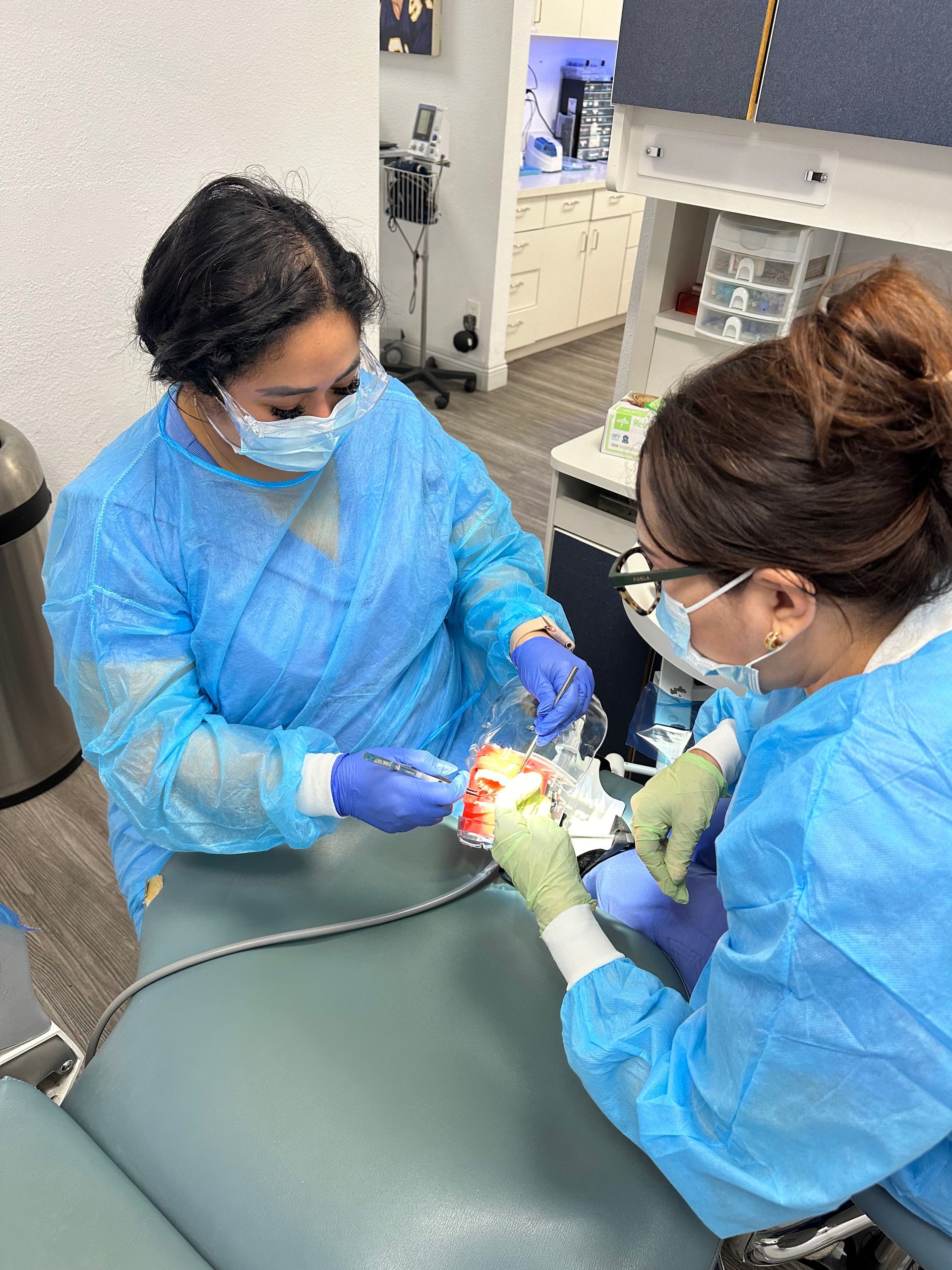 Two dental professionals in blue scrubs perform a procedure on a patient in a dental office.
