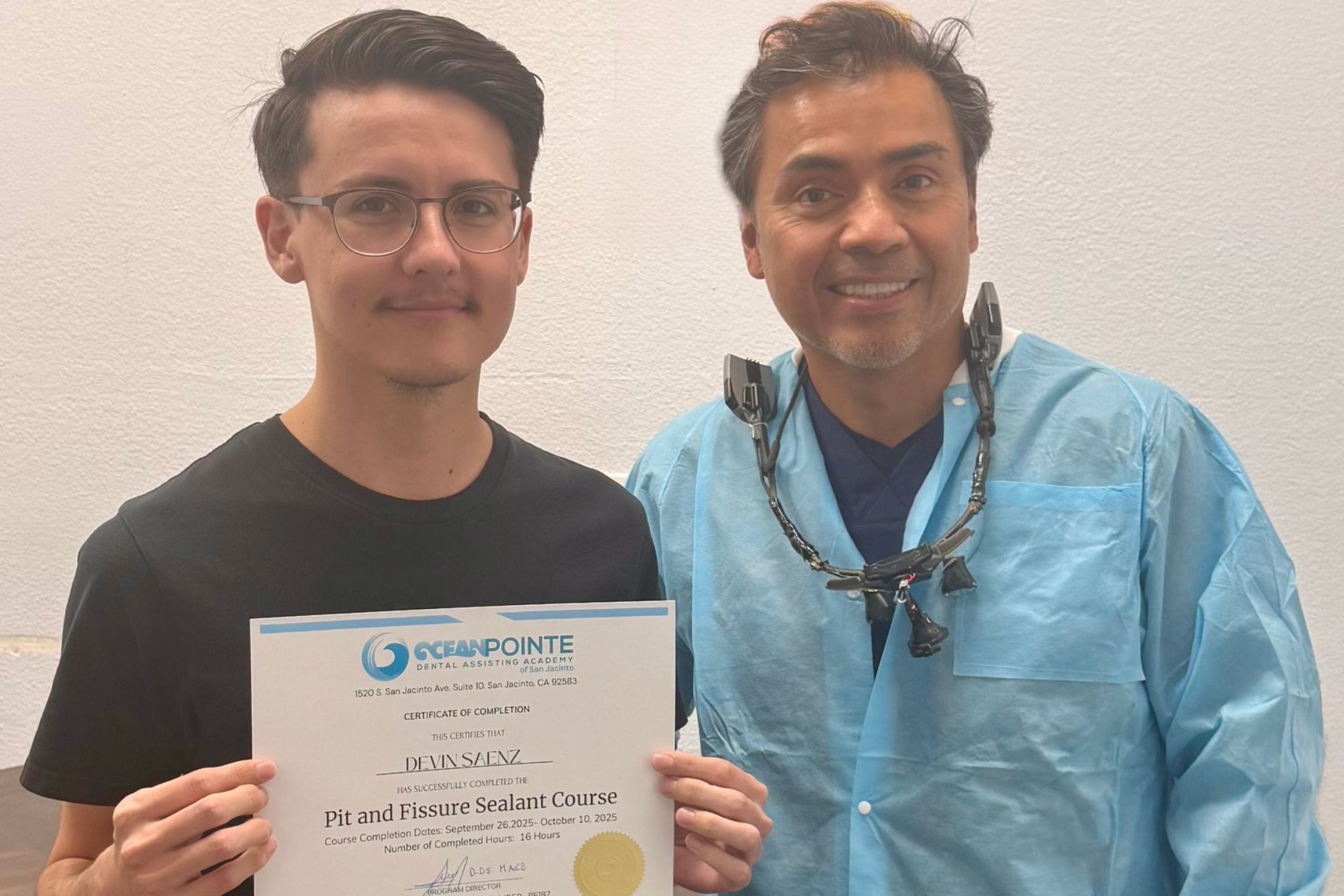 Smiling dental assistant in scrubs holding certificate in dental office.