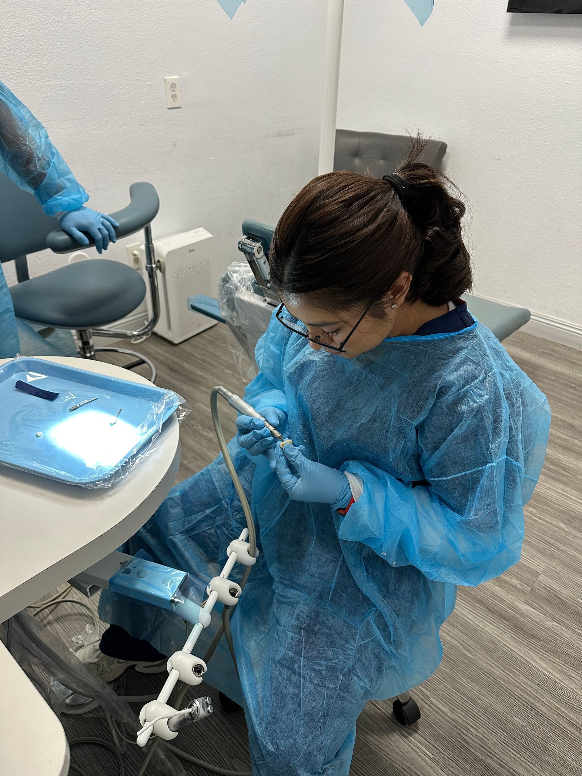 A dental assistant, wearing blue protective gear, assembling equipment in a dentist's office.