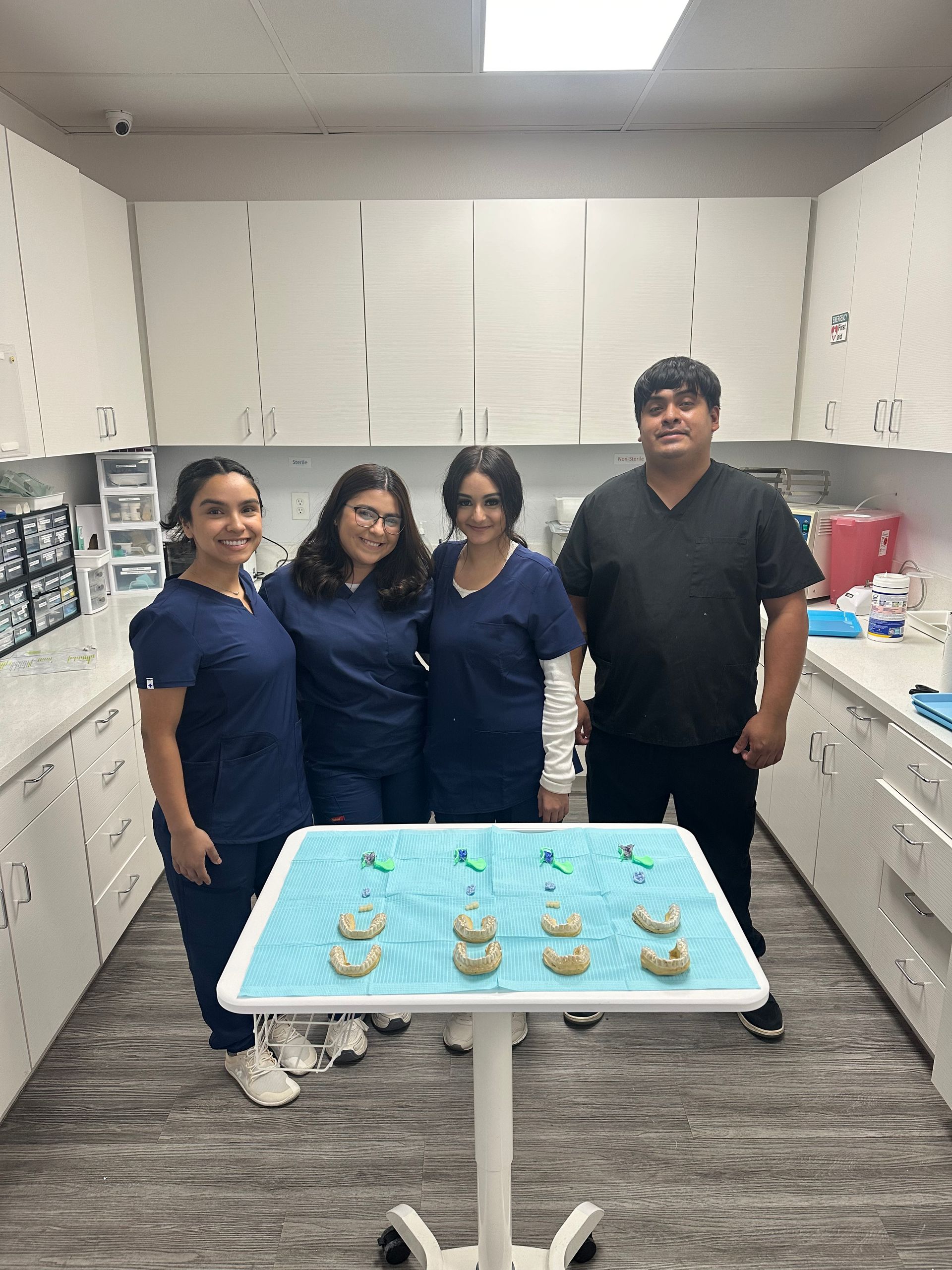 Four dental staff stand behind a table with dental molds in a clinic setting.