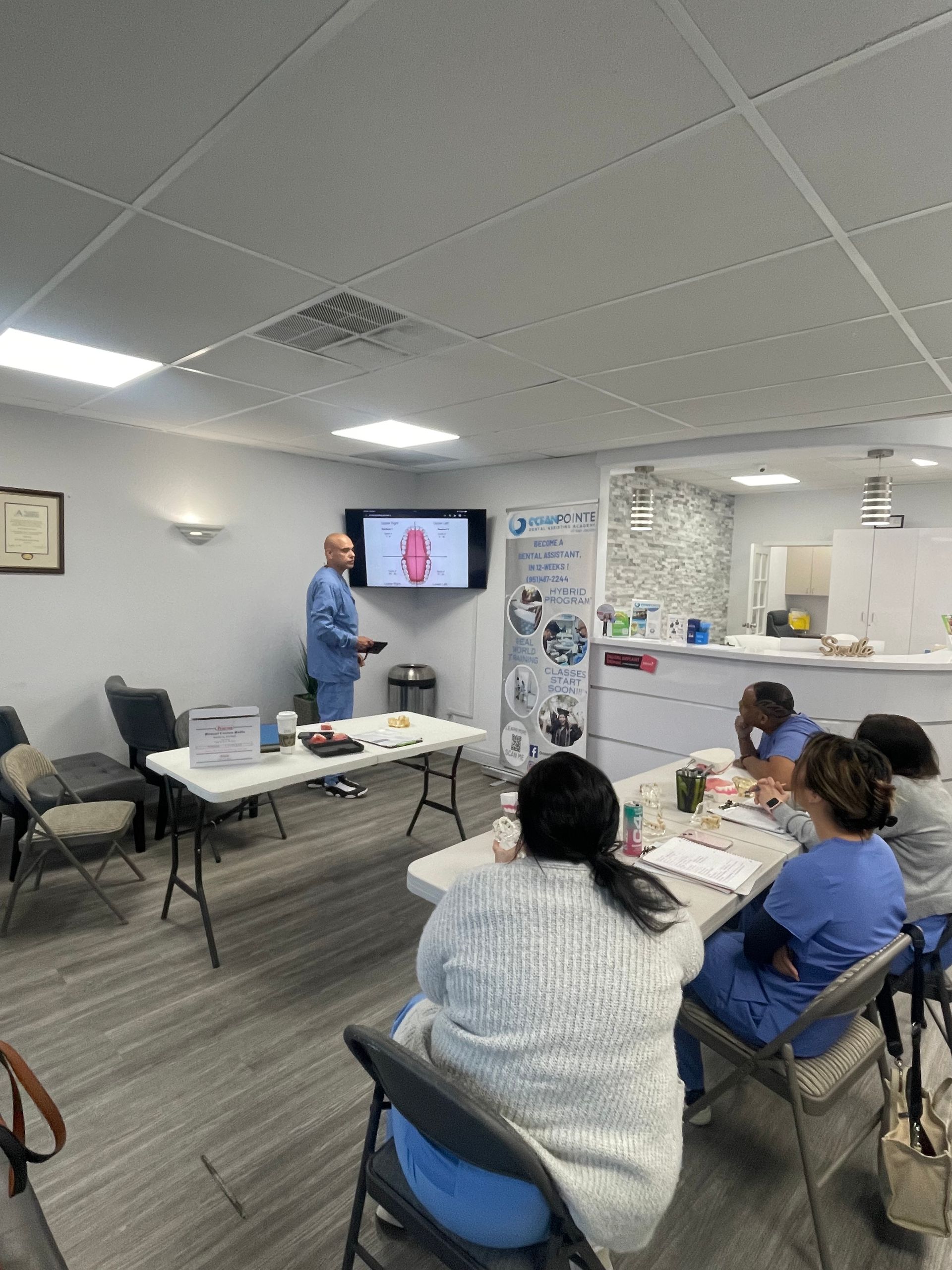 A man in scrubs presents to seated students in a well-lit classroom.
