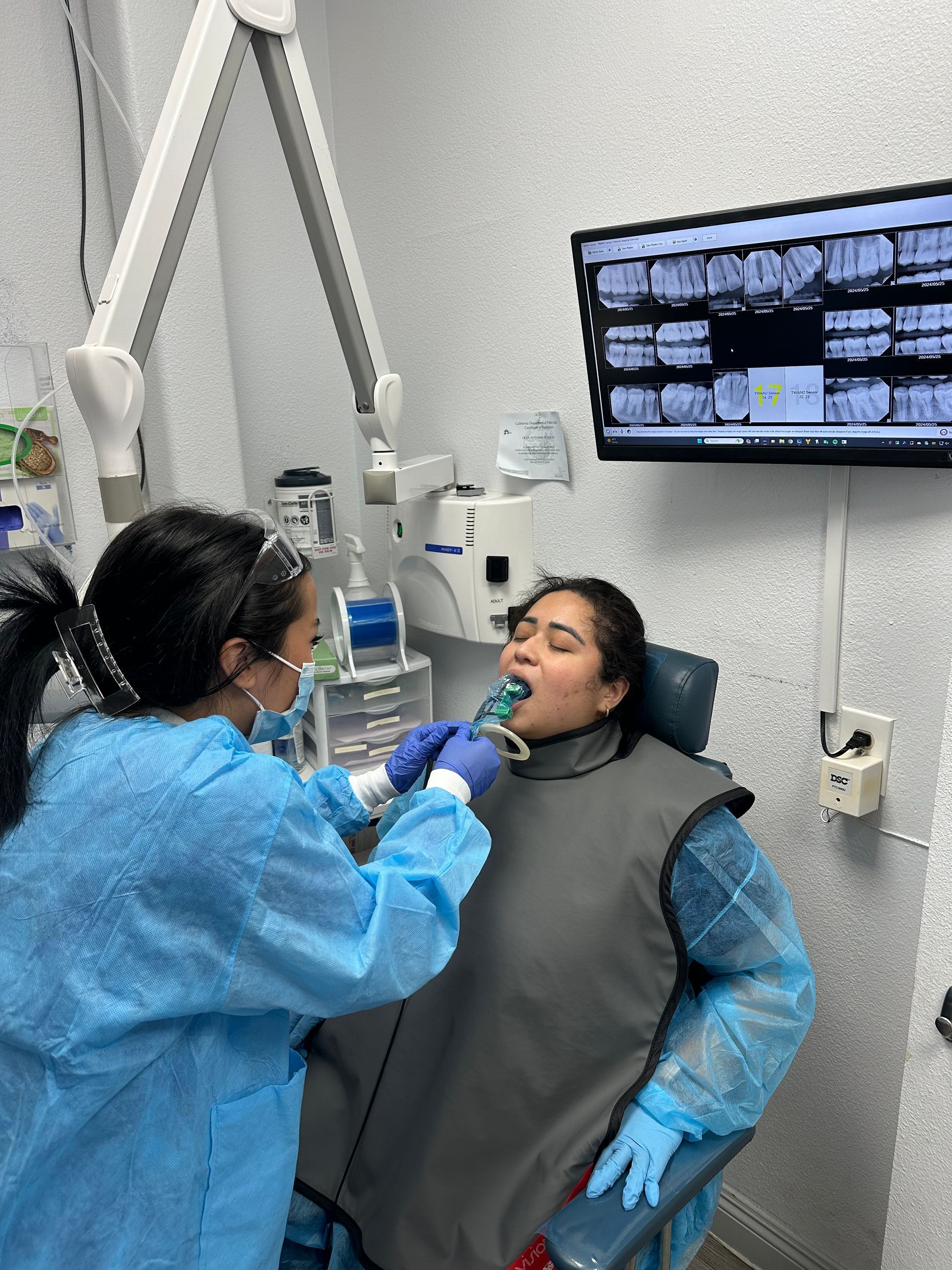 Dentist taking X-rays of a patient's teeth in an office; patient wears lead apron.