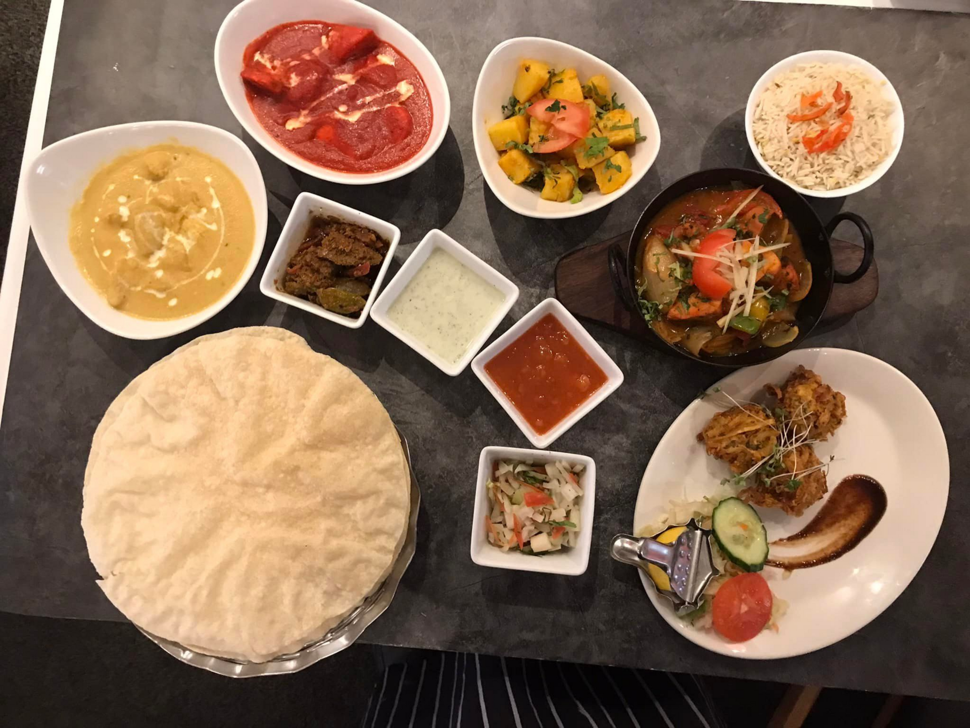 Indian meal on a table with papadums, dal, curry, salad, rice, chutneys, and a plate of grilled vegetables