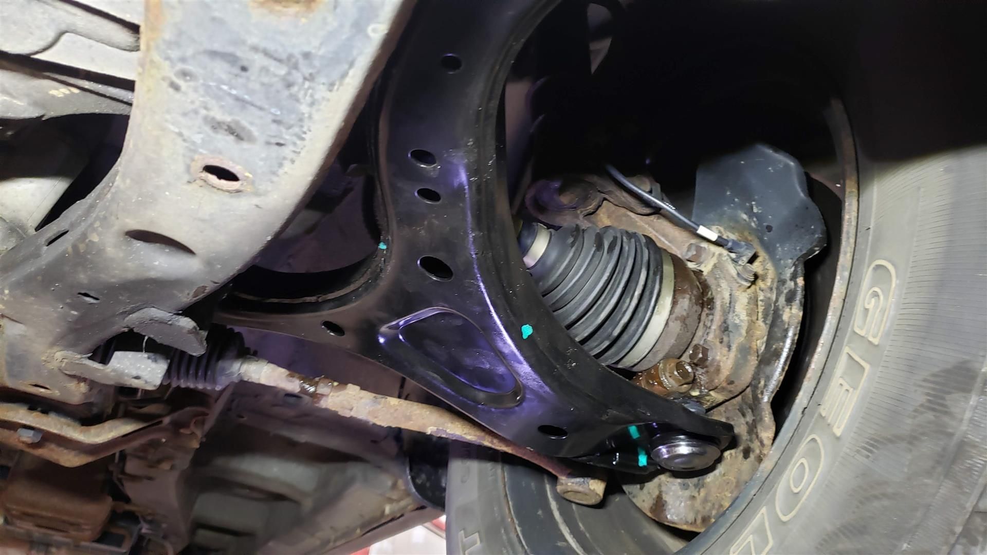 Undercarriage view: black control arm, CV axle, and wheel components of a vehicle.