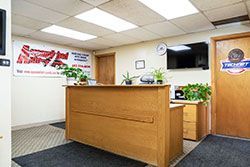 Reception desk in an office. Wooden counter, plants, TV, and sign on the wall.