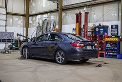 Dark blue sedan in an auto shop undergoing wheel alignment. Tools and shelves in background.