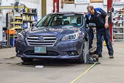 Mechanic adjusting a Subaru car's alignment in a garage.