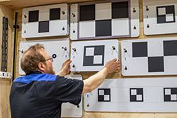 Man adjusting calibration targets on a wall; black and white checkerboard patterns.