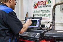 Mechanic using a diagnostic tool to examine a car's engine; workshop setting.