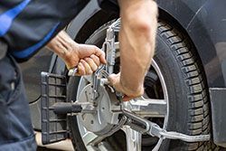 Mechanic adjusting car wheel alignment with a machine.