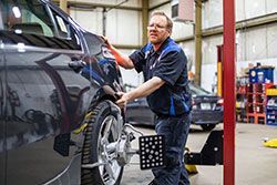 Mechanic adjusting car's wheel with alignment equipment inside a garage.