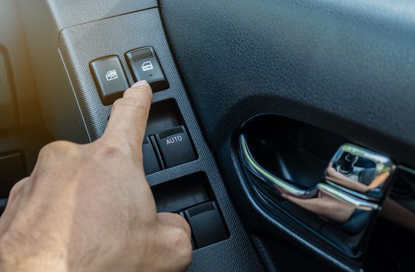 Hand pressing a car door lock button. Black interior with silver handle.
