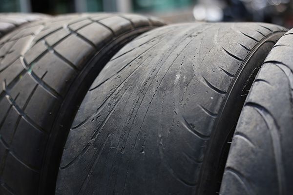 Four worn black tires close up, with shallow grooves. | Accomplished Automotive