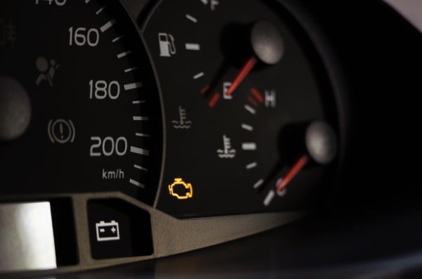 Car dashboard showing illuminated check engine light, battery, and temperature gauges.