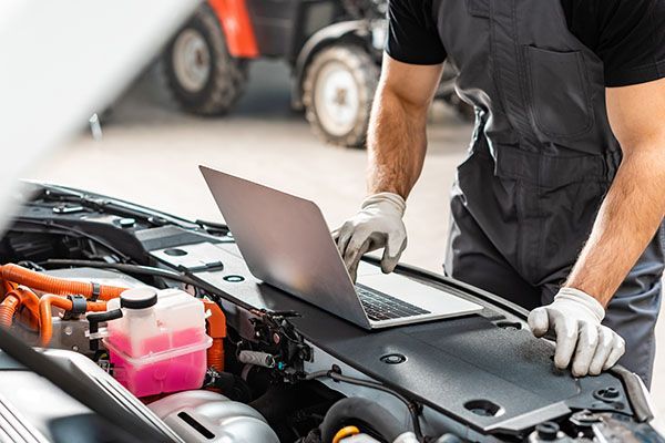 Mechanic using a laptop to diagnose a car engine.