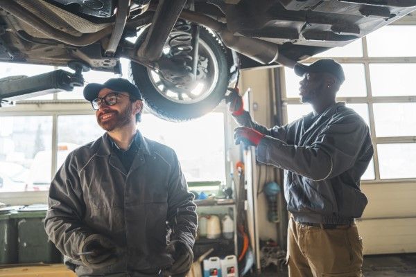 Two mechanics inspecting a car from underneath in a garage.