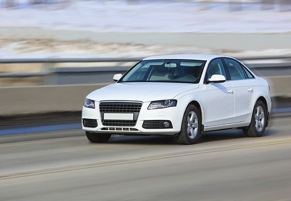 White sedan driving on a highway, possibly in winter.