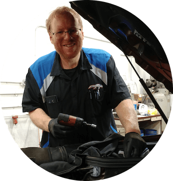 Mechanic smiles while holding a tool; working on a car with the hood up.