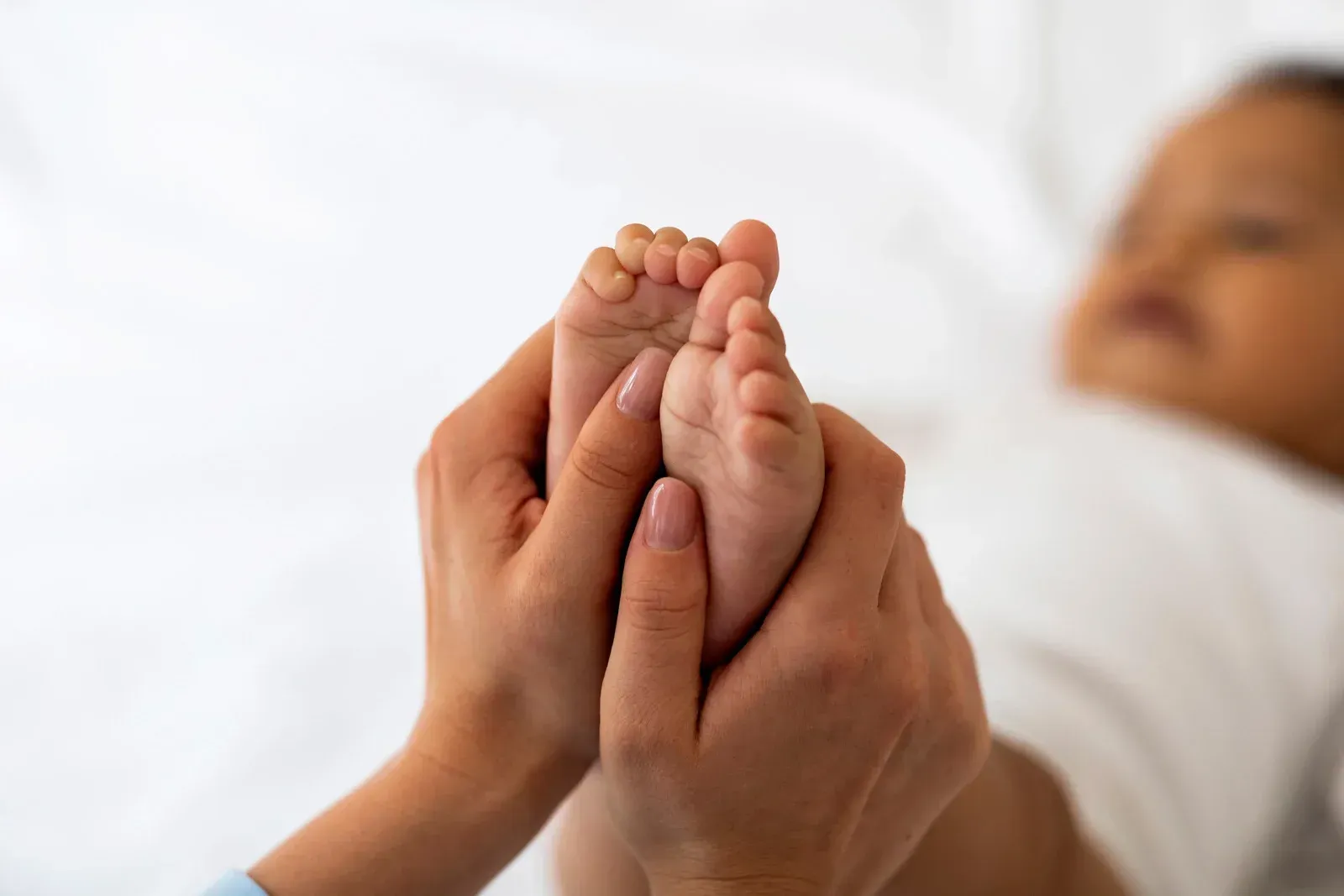 Hands gently holding a baby's tiny feet on a white surface.