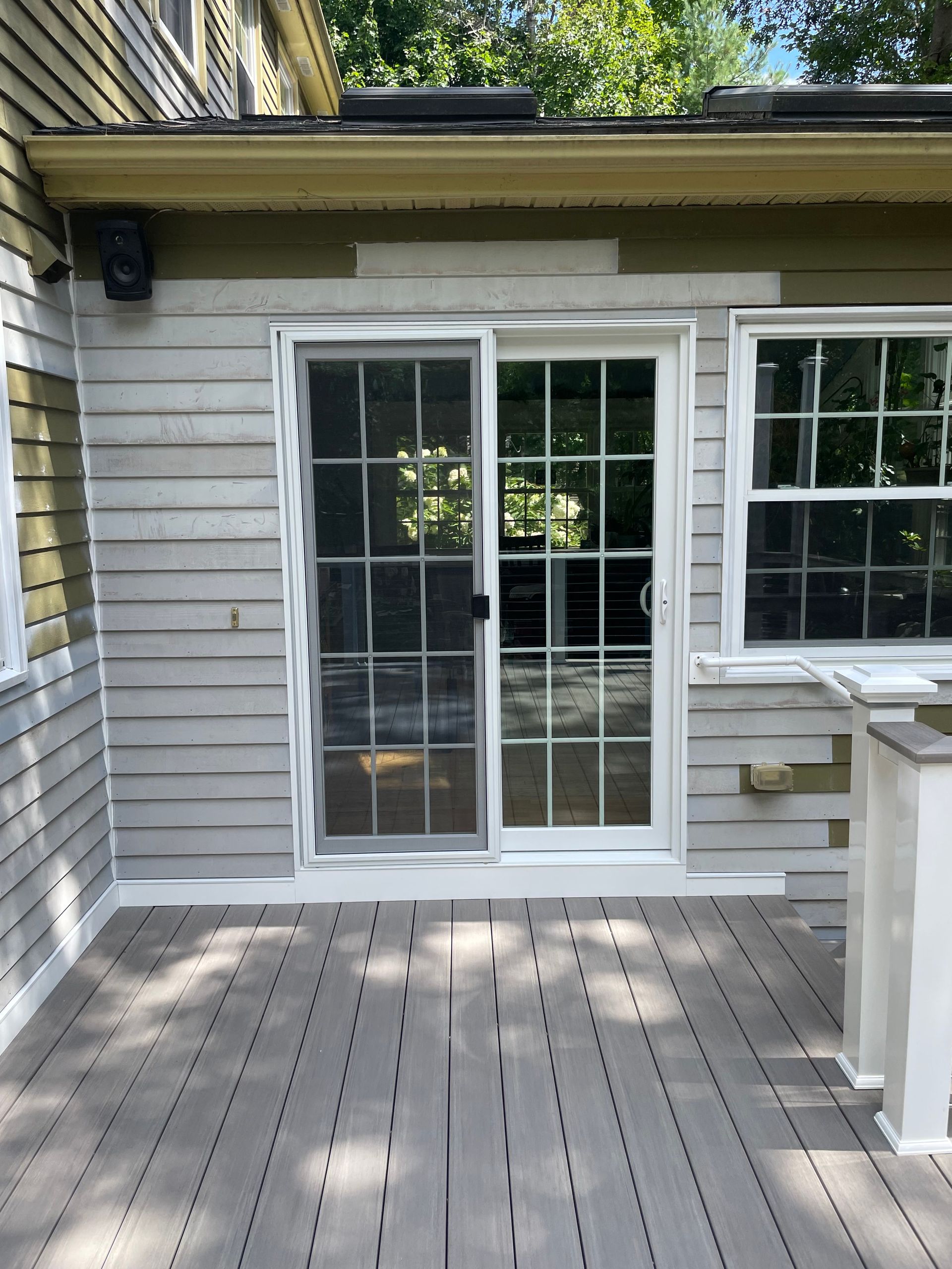 Wooden deck outside a gray house with white sliding glass doors and a railing on the right