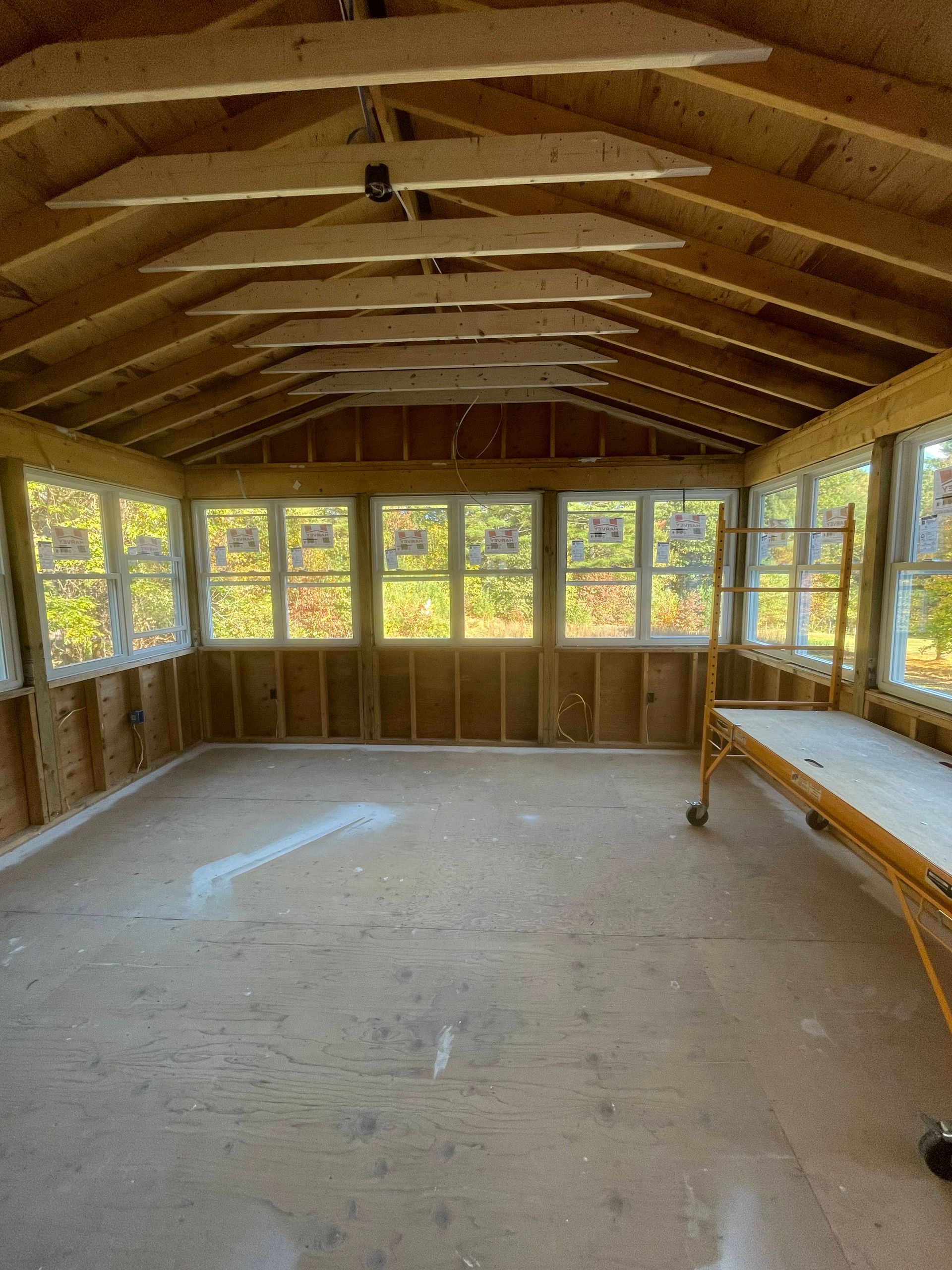 Empty sunroom with wood-paneled walls, exposed beams, and windows on three sides.