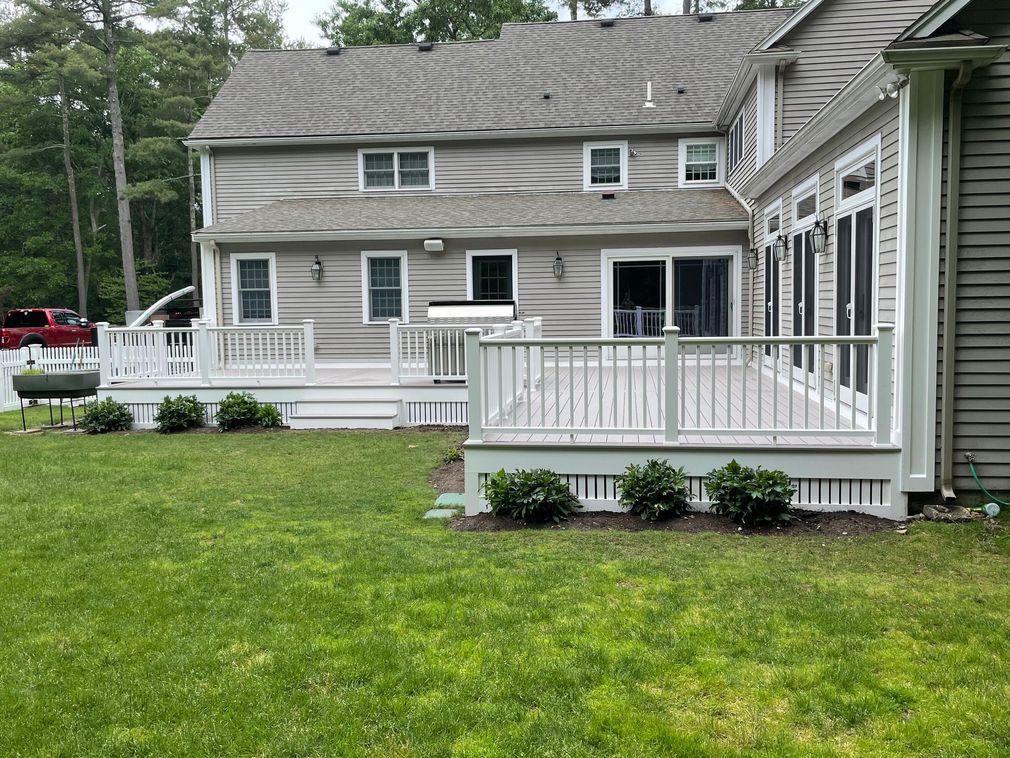 Backyard with gray house, white deck railings, and green lawn surrounded by trees