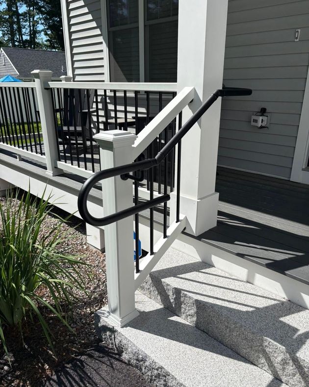 Front porch steps with white posts and black handrails beside a gray house entrance