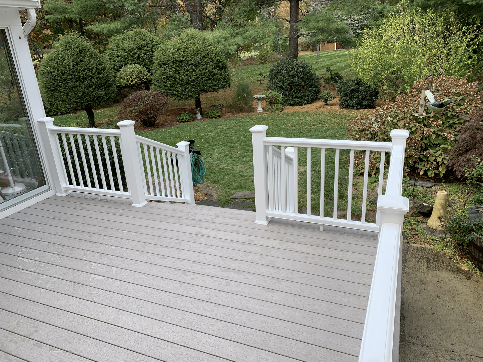 A deck with a white railing and a view of a garden.