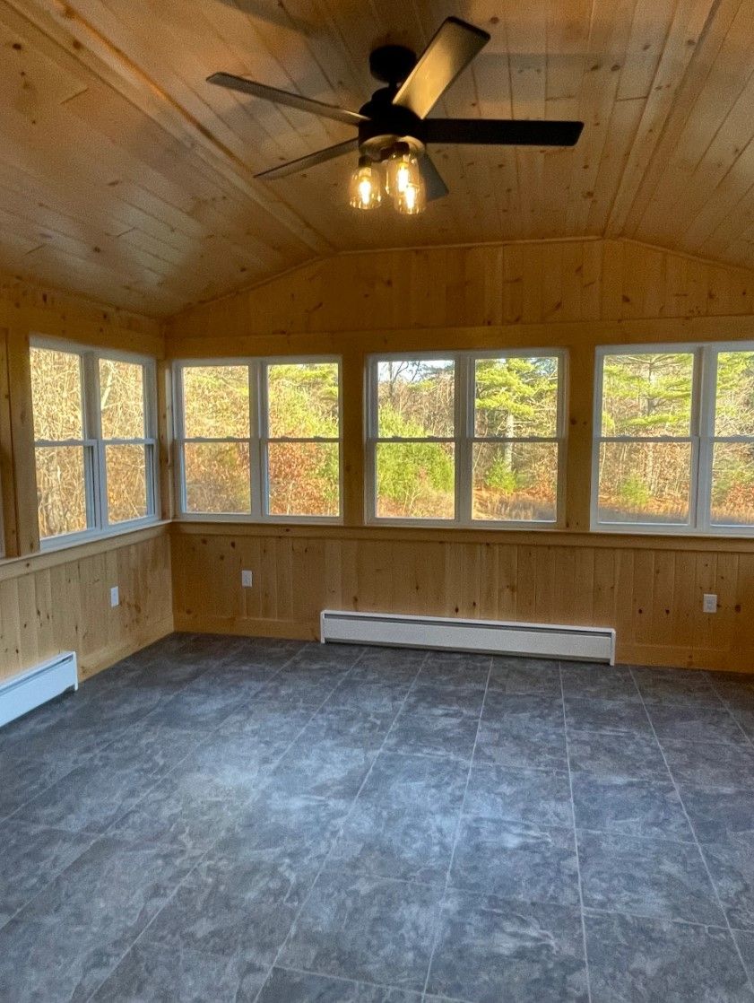 Sunroom with wood paneling, multiple windows, gray floor tiles, and a ceiling fan.