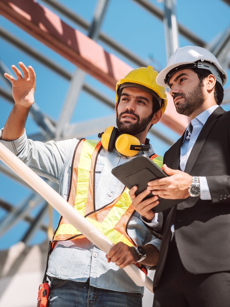 Two men are standing next to each other on a construction site looking at a tablet.