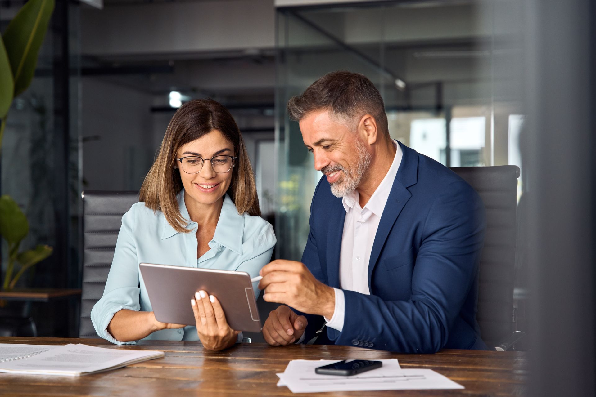 A man and a woman are sitting at a table looking at a tablet.