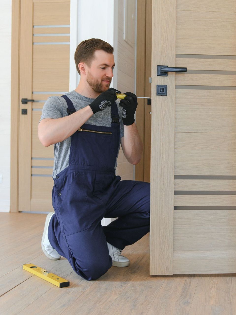 A man is kneeling down and fixing a door with a screwdriver.
