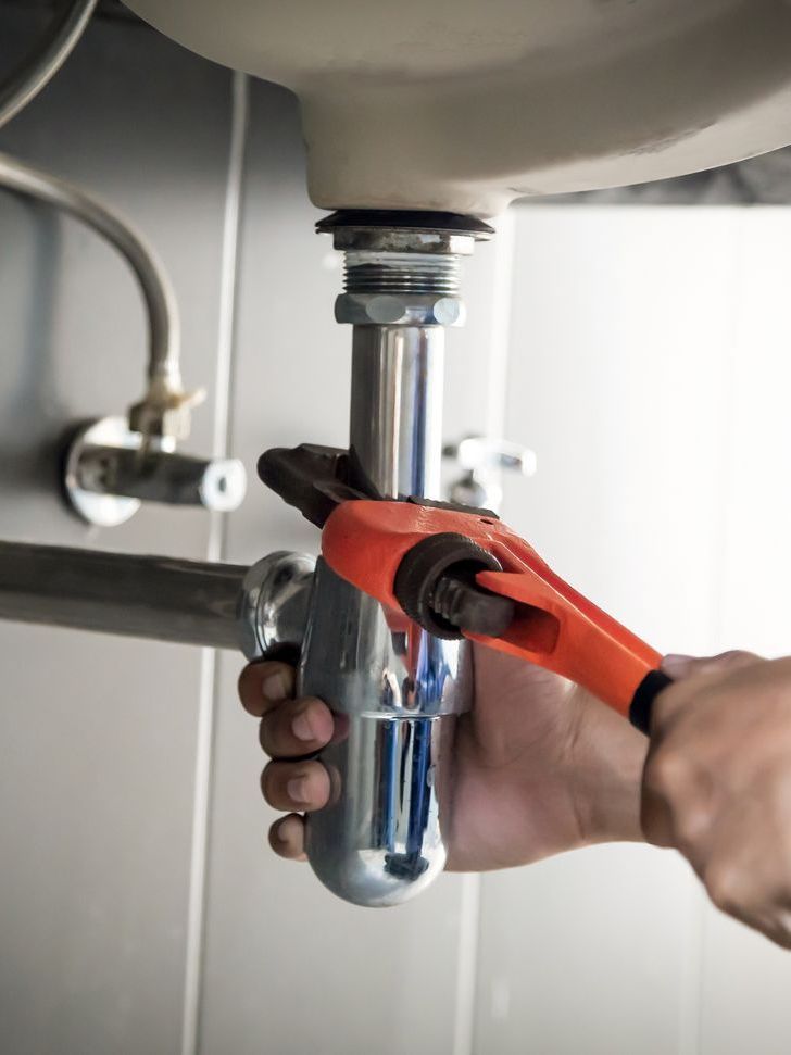 A person is fixing a sink pipe with a wrench.