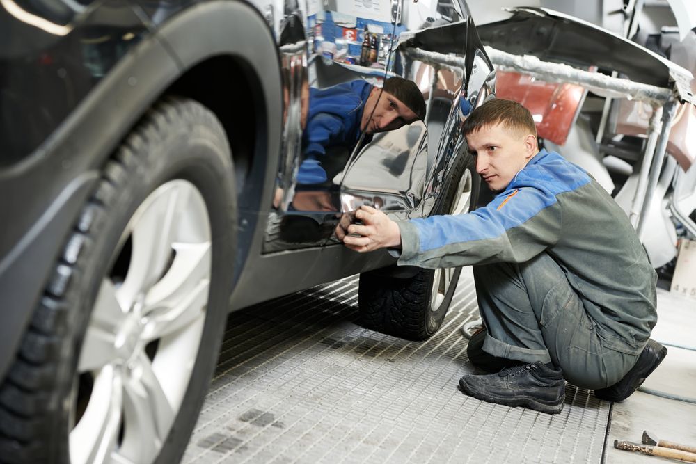 Mechanic examines a car door in a repair shop.